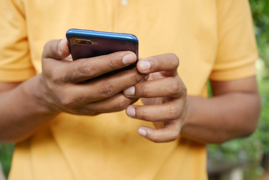 Close-up of a person in an orange shirt using a smartphone outdoors. — Photo by Towfiqu barbhuiya on Pexels